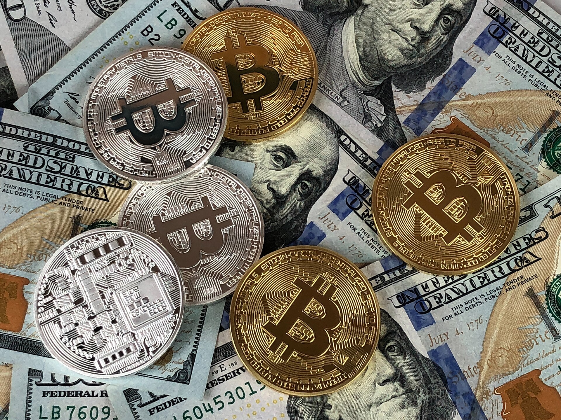 Gold and silver physical bitcoin tokens resting on US hundred-dollar bills